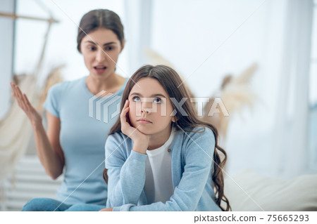 Nonlistening teenage girl turned away and mom behind 75665293