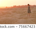 Young beautiful lonely smiling woman with long hair in long blue dress standing on sand at sunrise in hilly desert 75667423