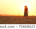 Elegant woman in long dress with straw hat standing on sand in desert, back view. Sunrise, backlight photo 75668025