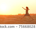 Elegant woman in long dress with straw hat junping elegant on sandy hills in desert. Sunrise, backlight photo 75668028