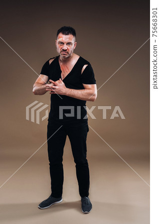 Against a gray background stands a battered angry man in a black T-shirt with wounds 75668301