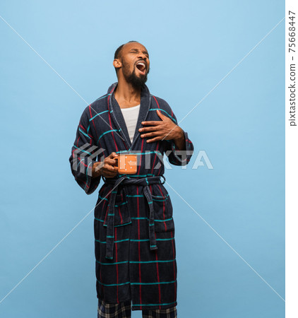 African-American man in bathrobe with cup of coffee isolated on blue background African-American man in bathrobe with cup of coffee isolated on blue background 75668447