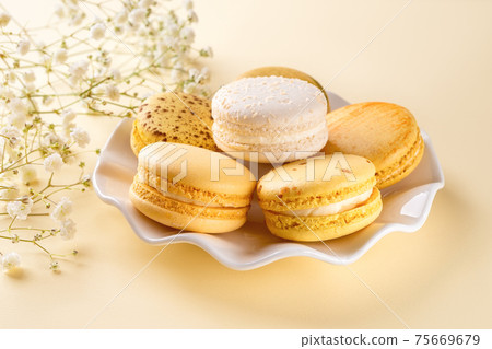Yellow macaroons on a white elegant saucer against pastel yellow background.  75669679