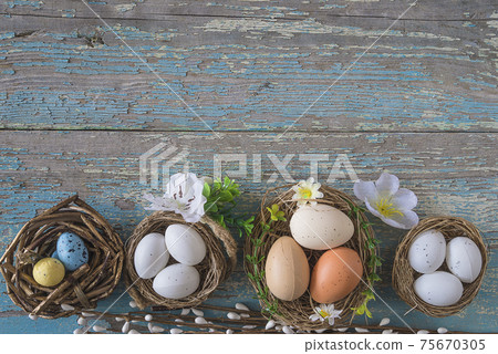 Happy Easter holiday background. Birdnests with eggs, flowers on old blue paint wooden background. Space for text, top view Happy Easter holiday background. Birdnests with eggs, flowers on old blue paint wooden background. Space for text, top view 75670305
