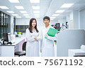 two young smiling scientist in white lab coat standing with automation blood analyzer at medical laboratory 75671192