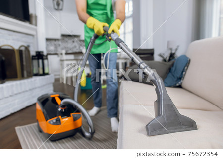 Close up of male janitor using vacuum cleaner for cleaning couch Close up of male janitor using vacuum cleaner for cleaning couch 75672354