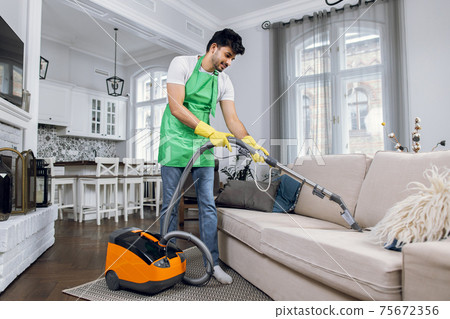 Indian man using vacuum cleaner for cleaning couch Indian man using vacuum cleaner for cleaning couch 75672356