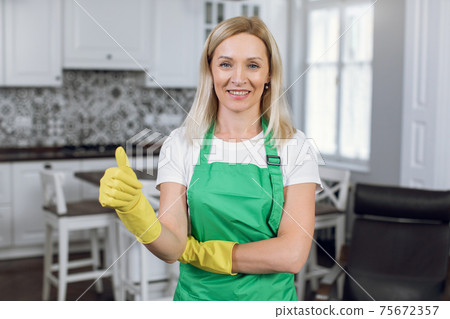 Beautiful housekeeper in green apron showing thumb up Beautiful housekeeper in green apron showing thumb up 75672357