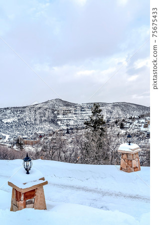Stone outdoor lamp post on terrain cobered with snow on a cloudy winter day 75675433