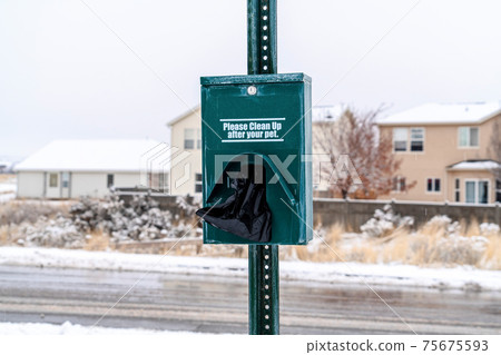 Dog waste station with black pet poop bags against snowy neighborhood landscape 75675593