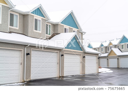 Apartment building exterior with white garages and pitched roofs against sky 75675665