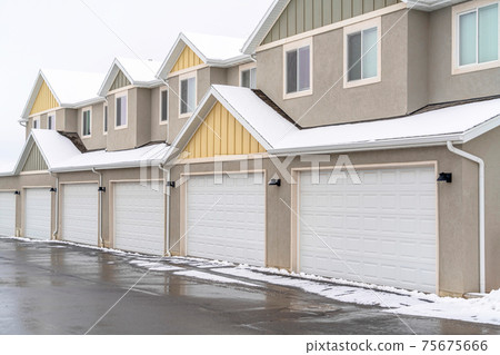 Wet road along white garage doors of apartment building against cloudy sky 75675666