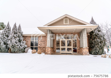 Building facade framed with lush snowy evergreens against cloudy sky in winter 75675786