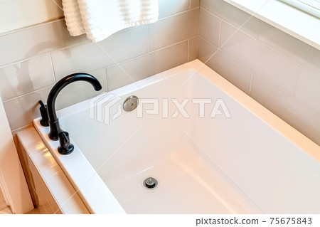 Rectangular built in bathtub with black curved faucet inside bathroom of home 75675843