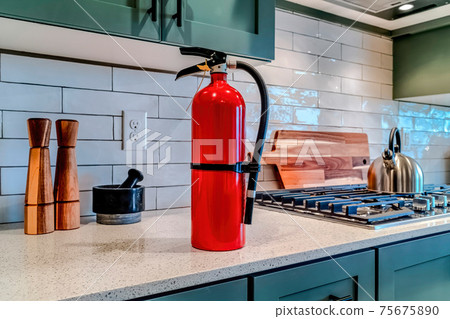 Red fire extinguisher beside cooktop on the countertop inside kitchen of home Red fire extinguisher beside cooktop on the countertop inside kitchen of home 75675890