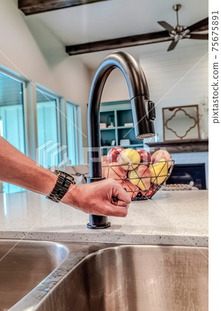 Man holding the lever of black curved faucet over stainless steel double sink 75675891