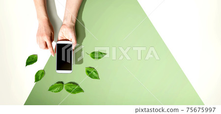 Person holding smartphone with green leaves 75675997
