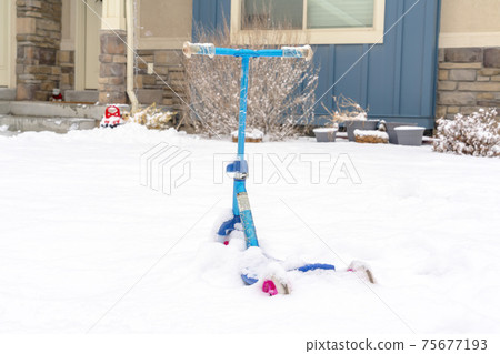 Colorful blue scooter on the snow covered front yard of home in winter 75677193
