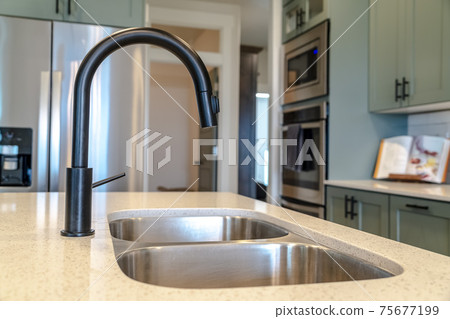 Kitchen island sink with double bowl and black faucet against kitchen appliances 75677199