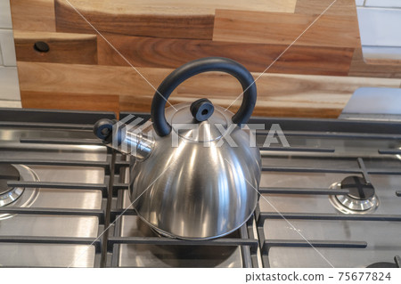 Kettle on the cooktop against wooden chopping board and tile backsplash Kettle on the cooktop against wooden chopping board and tile backsplash 75677824