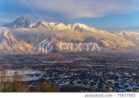 Mount Timpanogos over homes with snow at winter and illuminated by golden sunset Mount Timpanogos over homes with snow at winter and illuminated by golden sunset 75677883