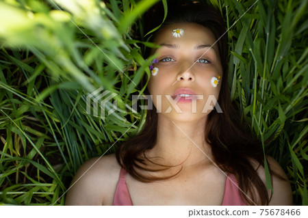 beautiful woman lies in green wheat with wild flowers and daisy glued on face beautiful woman lies in green wheat with wild flowers and daisy glued on face 75678466
