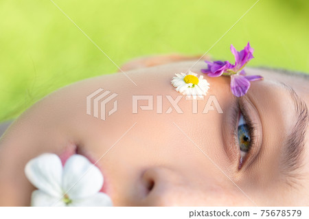 Macro shot Half of woman's beautiful face with wild flowers and daisy on skin 75678579