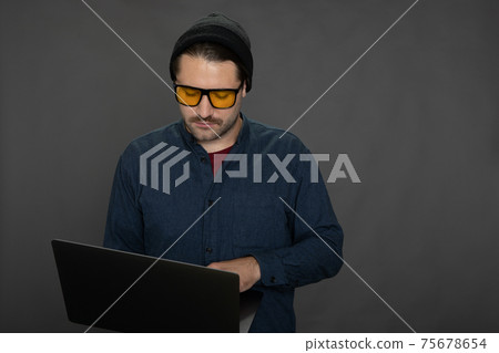 Handsome unshaven guy working with laptop on gray studio backdrop copy space 75678654