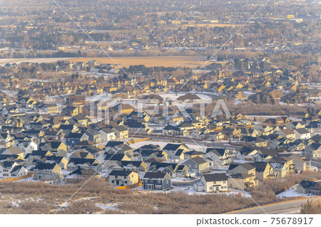 Tranquil neighborhood nestled amid hilly terrain covered with snow in winter 75678917