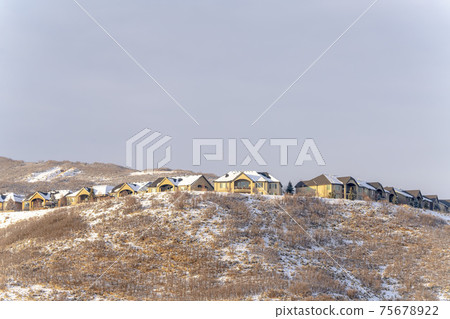 Snow covered hillly terrain with residential neighborhood against cloudy sky 75678922