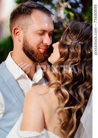 Happy and beautiful bride and groom gently cuddle in the park 75680699