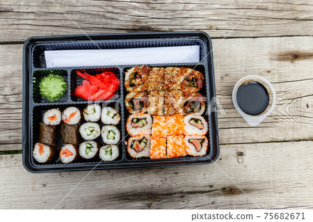 Set of sushi rolls in plastic box on wooden table. Sushi for take away or delivery of sushi in plastic container. Top view 75682671