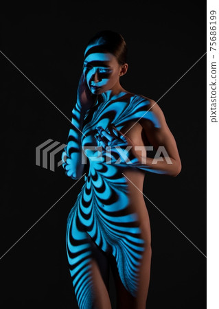 Nude woman standing in dark studio with striped illumination Nude woman standing in dark studio with striped illumination 75686199