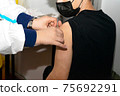 Doctor holding syringe and using cotton disk making injection to patient in medical mask. 75692291