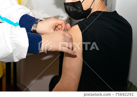 Doctor holding syringe and using cotton disk making injection to patient in medical mask. 75692291
