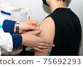 Doctor holding syringe and using cotton disk making injection to patient in medical mask. 75692293