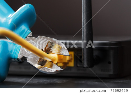 Tearing and cutting with blue wire cutters the network connection of the yellow wire of the Internet connection. Tearing and cutting with blue wire cutters the network connection of the yellow wire of the Internet connection. 75692439