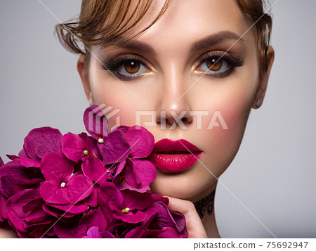Beautiful white girl with purple flowers. Stunning brunette girl with big violet bouquet flowers. Closeup face of young beautiful woman with a healthy clean skin. Pretty woman with bright makeup Beautiful white girl with purple flowers. Stunning brunette girl with big violet bouquet flowers. Closeup face of young beautiful woman with a healthy clean skin. Pretty woman with bright makeup 75692947