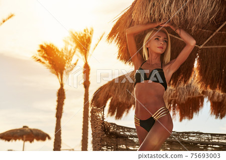 Woman standing nearby Cabana with straw roof on a sandy beach on sunny day at Red Sea Woman standing nearby Cabana with straw roof on a sandy beach on sunny day at Red Sea 75693003