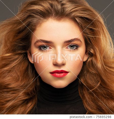 Closeup portrait of an young adult girl with long curly hair.  Photo of a fashion model posing at studio. Pretty young woman with red lips looking at camera. Beauty portrait. 75693298