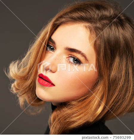 Closeup portrait of an young adult girl with medium length hair.  Photo of a fashion model posing at studio. Pretty young woman with red lips looking at camera. Beauty portrait. 75693299