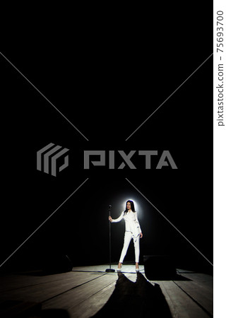 Singer woman on stage with black background in a beam of white light. Singer woman on stage with black background in a beam of white light. 75693700