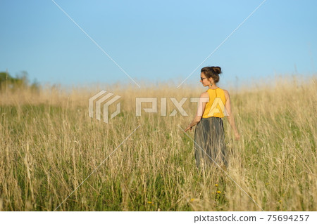 Beautiful woman in yellow shirt and long skirrt standing elegant in beige wheat field. Back view, bright blue sky Beautiful woman in yellow shirt and long skirrt standing elegant in beige wheat field. Back view, bright blue sky 75694257