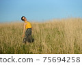 Beautiful woman in yellow shirt and long skirrt standing elegant in beige wheat field. Background of bright blue sky 75694258
