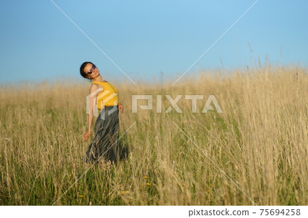 Beautiful woman in yellow shirt and long skirrt standing elegant in beige wheat field. Background of bright blue sky Beautiful woman in yellow shirt and long skirrt standing elegant in beige wheat field. Background of bright blue sky 75694258