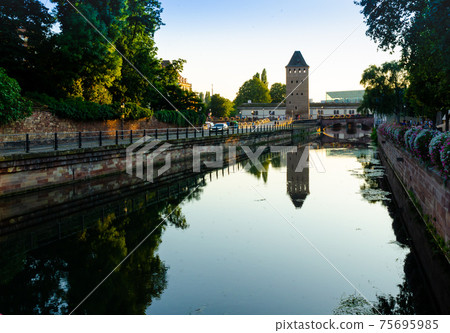 Strasbourg, France, August 2019. The historic center offers the view of pleasant and relaxing views: at dusk one of the towers of the covered bridges is reflected on the canal. Strasbourg, France, August 2019. The historic center offers the view of pleasant and relaxing views: at dusk one of the towers of the covered bridges is reflected on the canal. 75695985