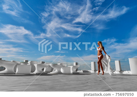 The young woman in white pareo on a terrace and blue sky on a background The young woman in white pareo on a terrace and blue sky on a background 75697050