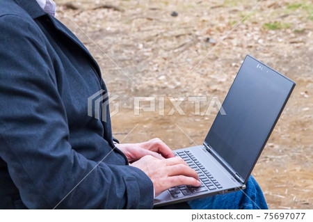 A man typing a computer in the park 75697077