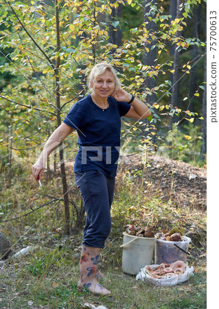 A girl with a knife in her hand stands next to buckets of mushrooms 75700613