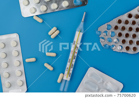 Mercury thermometer, white capsules and tablets in a package on blue background 75700620